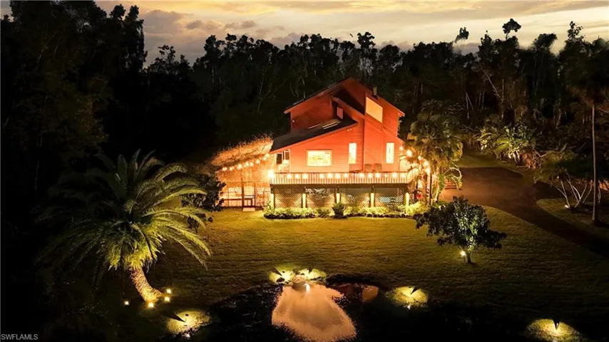 house at dusk featuring a lawn and pond