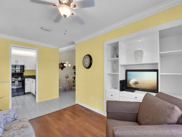 Living room with crown molding, ceiling fan, light wood-style floors, a chandelier, and built in features