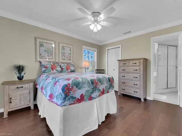 Bedroom featuring ornamental molding, dark wood-style flooring, a closet, ensuite bath, and a ceiling fan