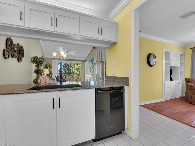 Kitchen featuring crown molding, dark stone countertops, white cabinetry, black dishwasher, and light tile patterned floors