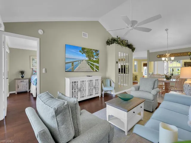 Living room featuring crown molding, lofted ceiling, wood finished floors, ceiling fan, and a chandelier