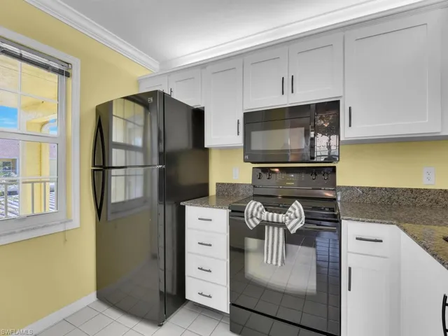 Kitchen with black appliances, dark stone countertops, ornamental molding, light tile patterned floors, and white cabinets