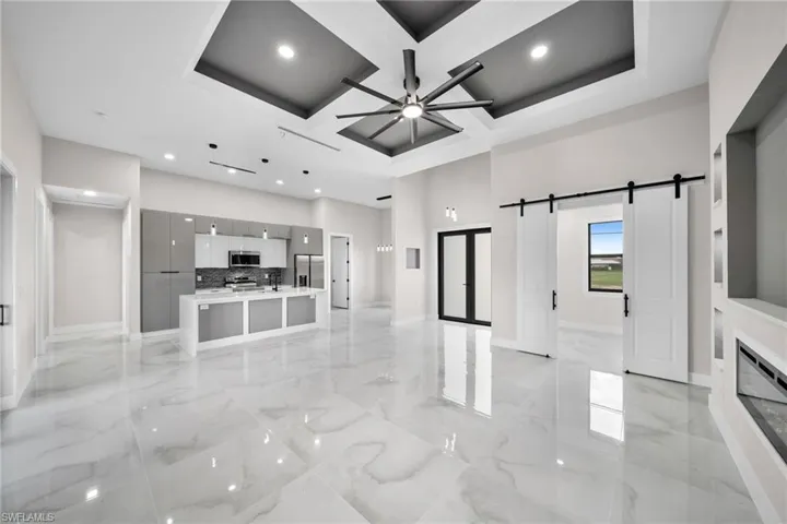 Unfurnished living room featuring coffered ceiling, light tile patterned flooring, beam ceiling, ceiling fan, and a barn door