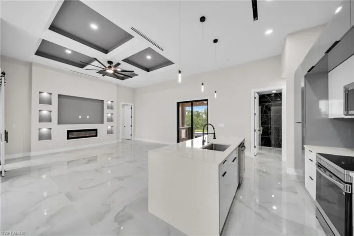 Kitchen featuring coffered ceiling, pendant lighting, appliances with stainless steel finishes, a center island with sink, and ceiling fan