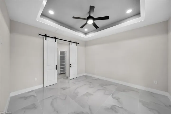 Unfurnished bedroom featuring ceiling fan, a barn door, a raised ceiling, and light tile patterned floors