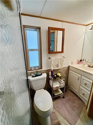 Bathroom with wainscoting, vanity, tile walls, a textured ceiling, and crown molding