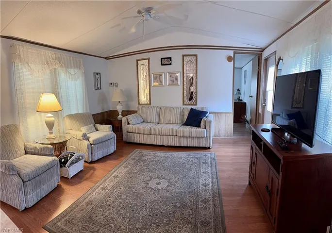 Living room featuring wainscoting, ceiling fan, vaulted ceiling, wood vinyl floors, and wainscoting.