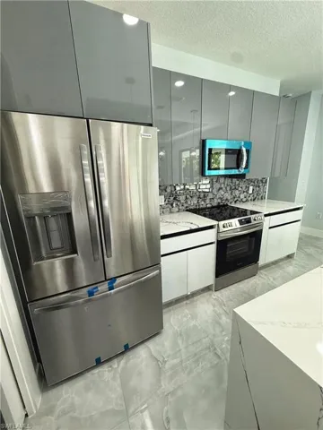 Kitchen with stainless steel appliances, modern cabinets, light marble finish flooring, a textured ceiling, and light stone countertops