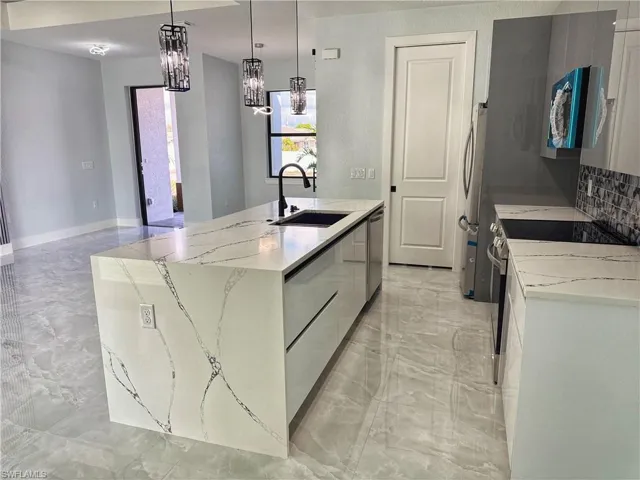 Kitchen with light stone countertops, stainless steel appliances, a kitchen island with sink, and light marble finish flooring