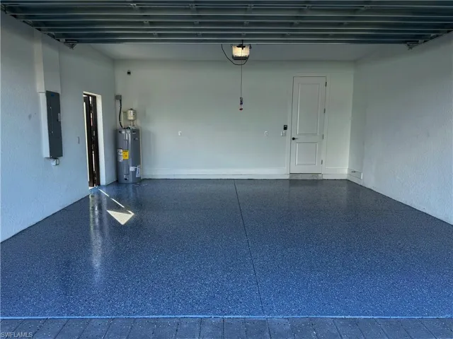 Garage with electric water heater, electric panel, and a garage door opener