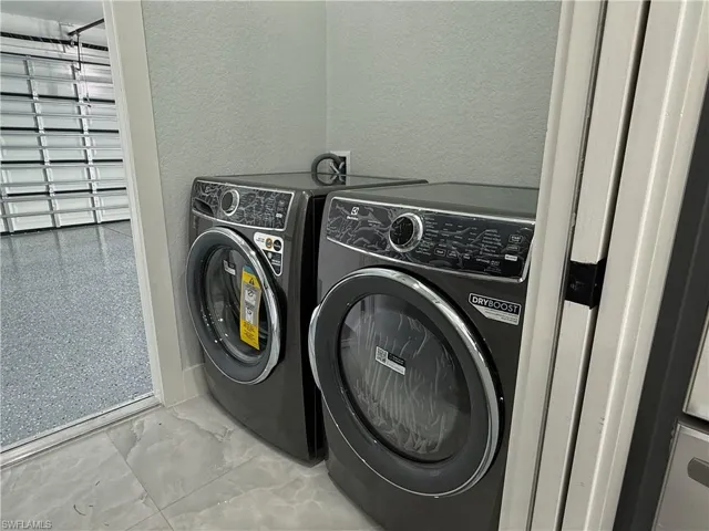 Laundry area featuring a textured wall, washing machine and dryer, and light marble finish flooring