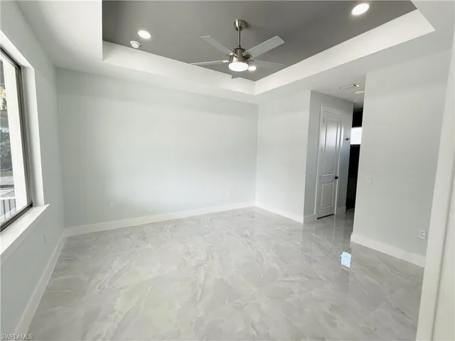 Empty room featuring a raised ceiling, ceiling fan, recessed lighting, plenty of natural light, and light marble finish flooring