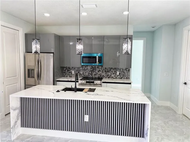 Kitchen with light stone countertops, stainless steel appliances, decorative backsplash, and modern cabinets