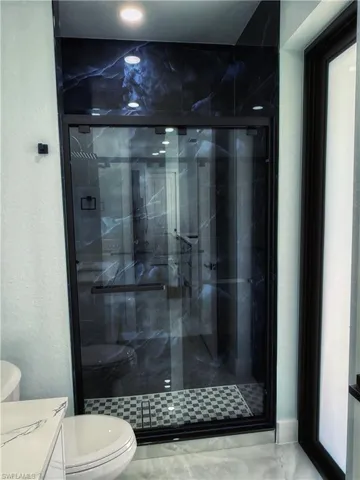 Bathroom featuring a marble finish shower, a textured wall, and vanity