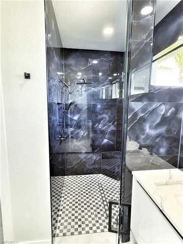 Bathroom with vanity, a marble finish shower, and a textured wall