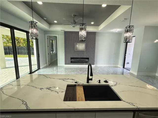 Kitchen featuring light stone countertops, a ceiling fan, light marble finish floors, suspended lighting, and a tray ceiling