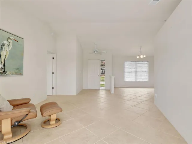 Sitting room with ceiling fan with notable chandelier, light tile patterned floors, and vaulted ceiling