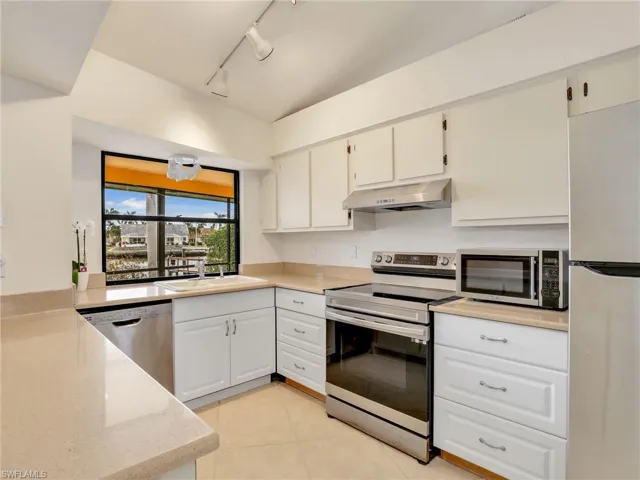 Kitchen with appliances with stainless steel finishes, track lighting, sink, light tile patterned floors, and white cabinetry