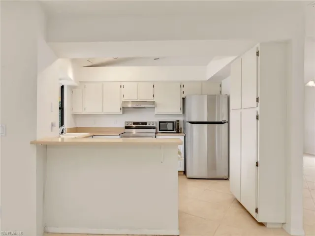 Kitchen with kitchen peninsula, sink, light tile patterned flooring, and appliances with stainless steel finishes