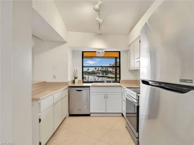 Kitchen with rail lighting, stainless steel appliances, sink, white cabinets, and light tile patterned flooring