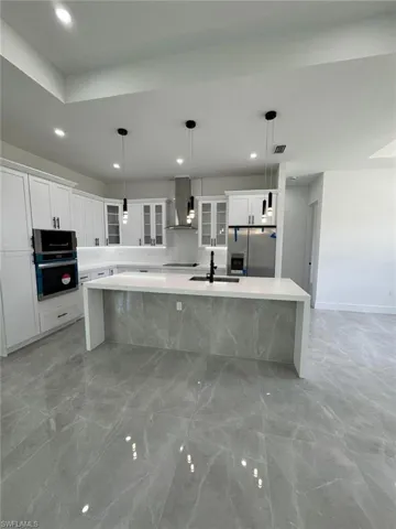 Kitchen with glass insert cabinets, a spacious island, light stone countertops, white cabinets, and stainless steel appliances