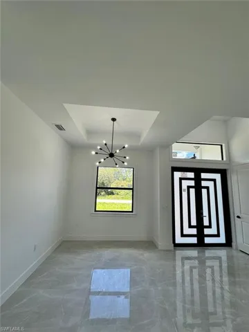 Unfurnished dining area featuring a raised ceiling, a chandelier, and light marble finish flooring