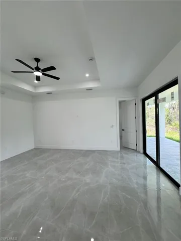 Spare room featuring a tray ceiling, a ceiling fan, and light marble finish flooring