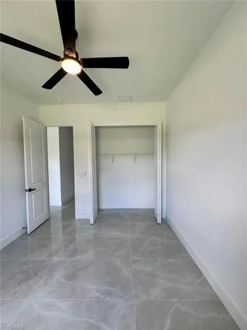 Unfurnished bedroom with a ceiling fan, light marble finish flooring, and a closet