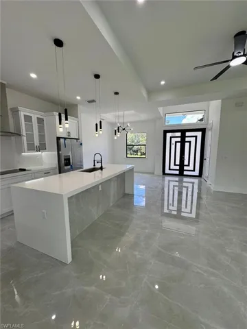 Kitchen featuring light marble finish flooring, white cabinets, glass insert cabinets, a large island with sink, and recessed lighting