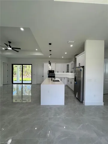 Kitchen featuring open floor plan, white cabinets, light marble finish flooring, pendant lighting, and appliances with stainless steel finishes