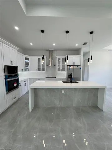 Kitchen with glass insert cabinets, a spacious island, light stone countertops, a kitchen breakfast bar, and pendant lighting