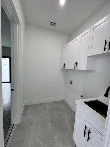 Washroom with hookup for an electric dryer, hookup for a washing machine, cabinet space, and light marble finish flooring
