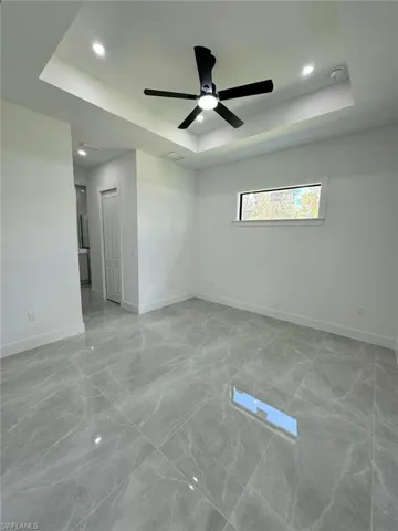 Empty room with a tray ceiling, recessed lighting, light marble finish floors, and a ceiling fan