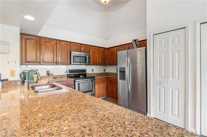 Kitchen featuring light stone counters, stainless steel appliances, brown cabinets, and recessed lighting
