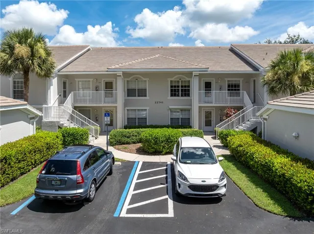 View of property with stairs and uncovered parking