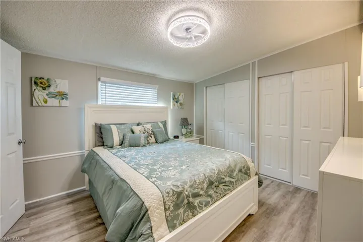 Bedroom with light wood-type flooring, multiple closets, a textured ceiling, vaulted ceiling, and crown molding