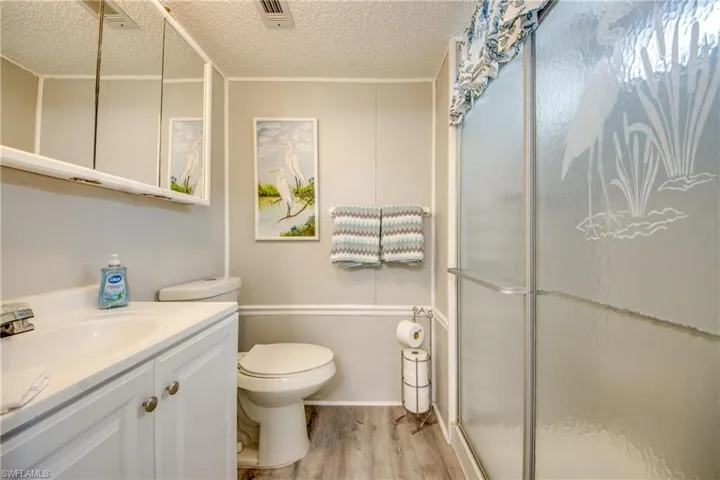 Full bath with vanity, a stall shower, a textured ceiling, and light wood-style flooring