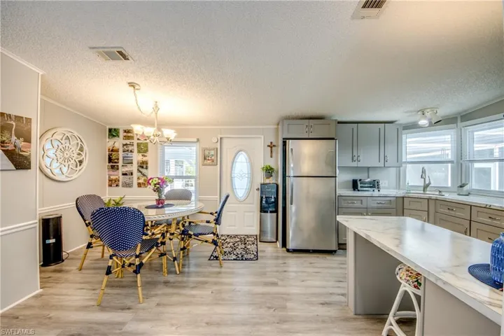 Kitchen featuring gray cabinets, freestanding refrigerator, a textured ceiling, light wood-type flooring, and a chandelier