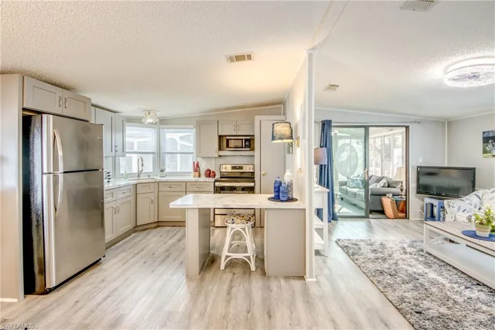 Kitchen with stainless steel appliances, a textured ceiling, light wood-style flooring, open floor plan, and a kitchen bar