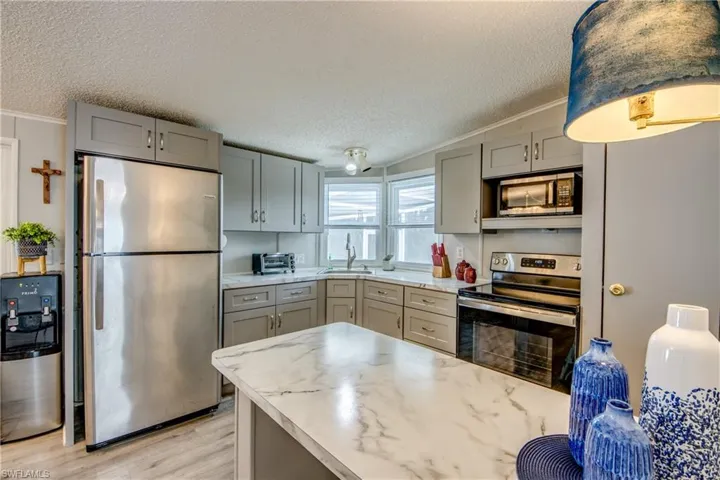 Kitchen featuring appliances with stainless steel finishes, gray cabinetry, light countertops, a textured ceiling, and light wood-style floors