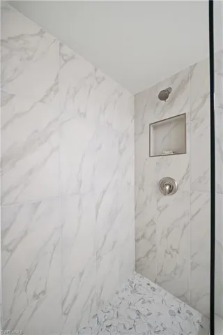 Shower stall featuring large format white tile with grey veining, a built-in shower niche, and a contrasting mosaic tile floor