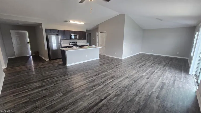 Kitchen featuring open floor plan, appliances with stainless steel finishes, dark wood-type flooring, and vaulted ceiling