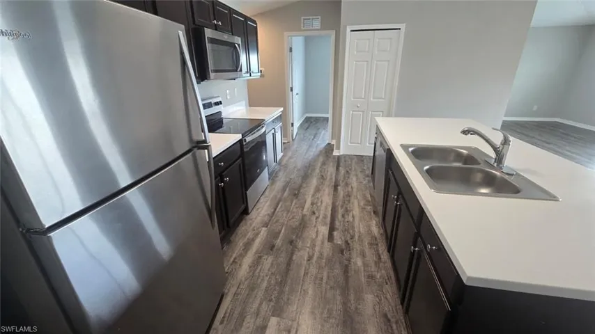 Kitchen featuring dark cabinetry, light countertops, stainless steel appliances, dark wood-style flooring, and vaulted ceiling