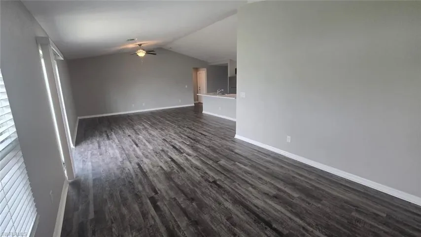 Unfurnished living room with dark wood-style floors, vaulted ceiling, and ceiling fan