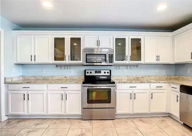 Kitchen featuring light tile patterned flooring, white cabinetry, light stone countertops, and appliances with stainless steel finishes