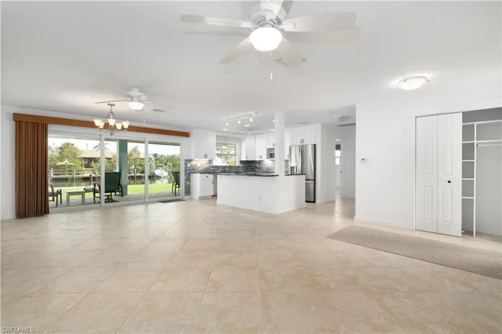 Kitchen featuring white cabinetry, backsplash, stainless steel fridge, and ceiling fan with notable chandelier