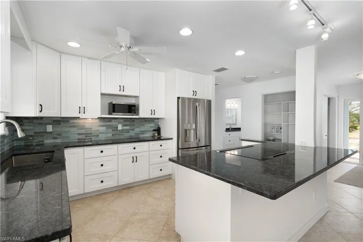 Kitchen featuring white cabinets, appliances with stainless steel finishes, dark stone counters, and sink