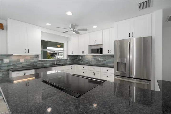 Kitchen with dark stone countertops, white cabinetry, and appliances with stainless steel finishes