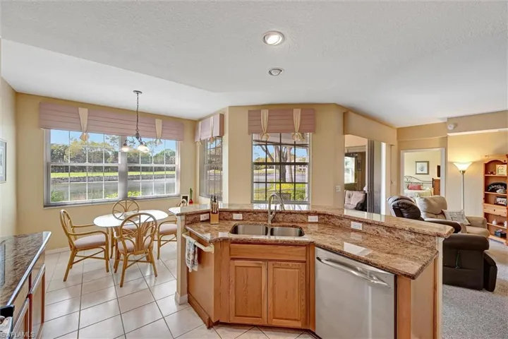 Kitchen featuring light tile patterned flooring, a sink, open floor plan, light stone countertops, and dishwasher