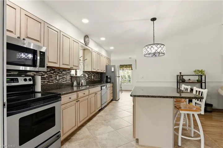 Kitchen with stainless steel appliances, a breakfast bar area, dark stone counters, hanging light fixtures, and backsplash